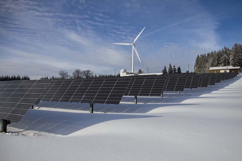 Solaranlage und Windrad in einer Schneelandschaft. Symbolbild für nachhaltiges Investieren.