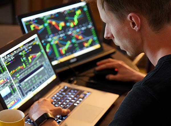 Daytrading erklärt. Mann sitzt vor einem Laptop, auf dem Börsenkurse angezeigt werden. Er ist Trader.